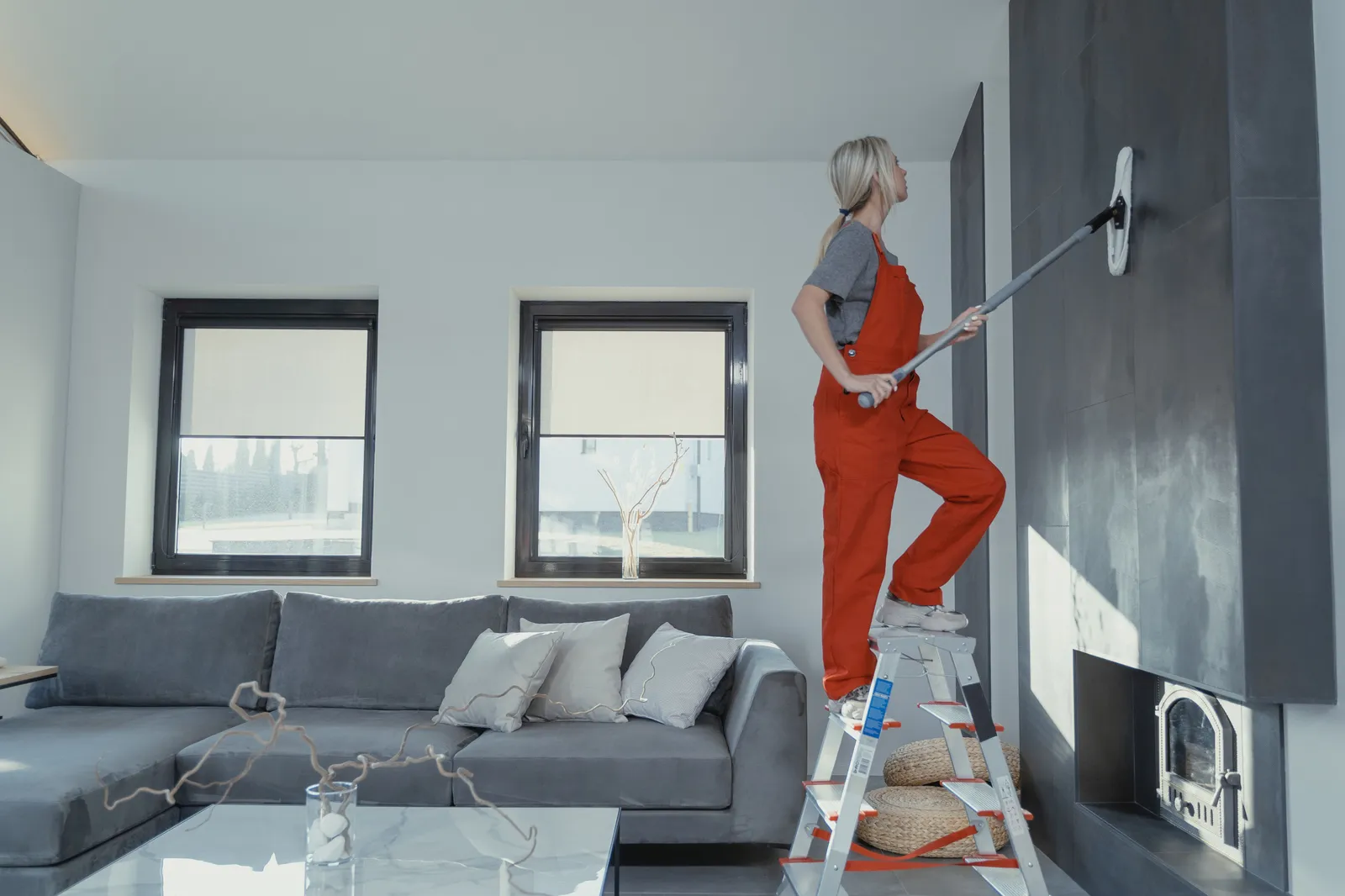 A cleaner on a ladder wiping down a tall tiled accent wall